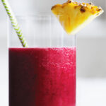 Close up glass of beet pineapple juice with a slice of pineapple