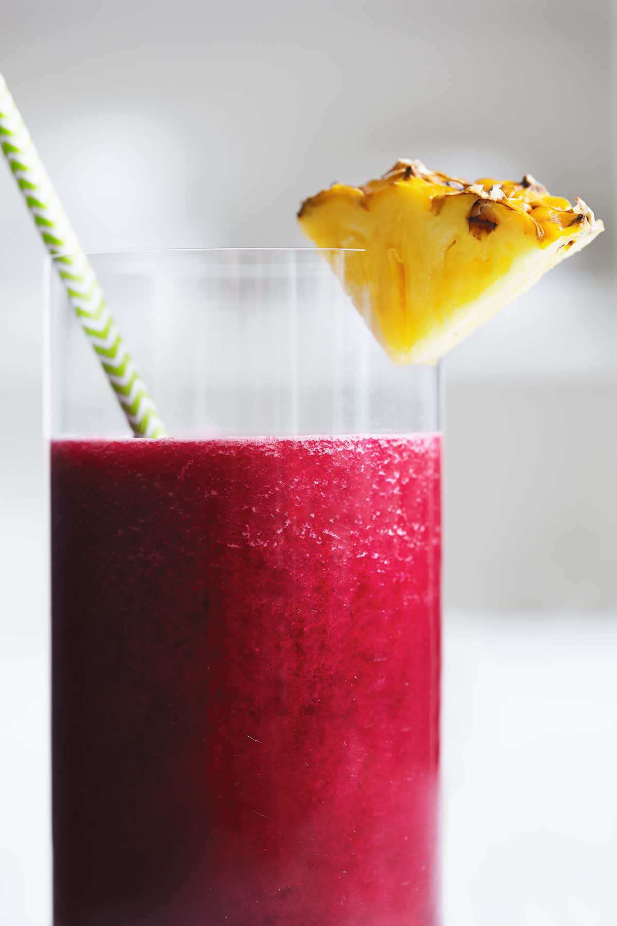 Close up glass of beet pineapple juice with a slice of pineapple and straw