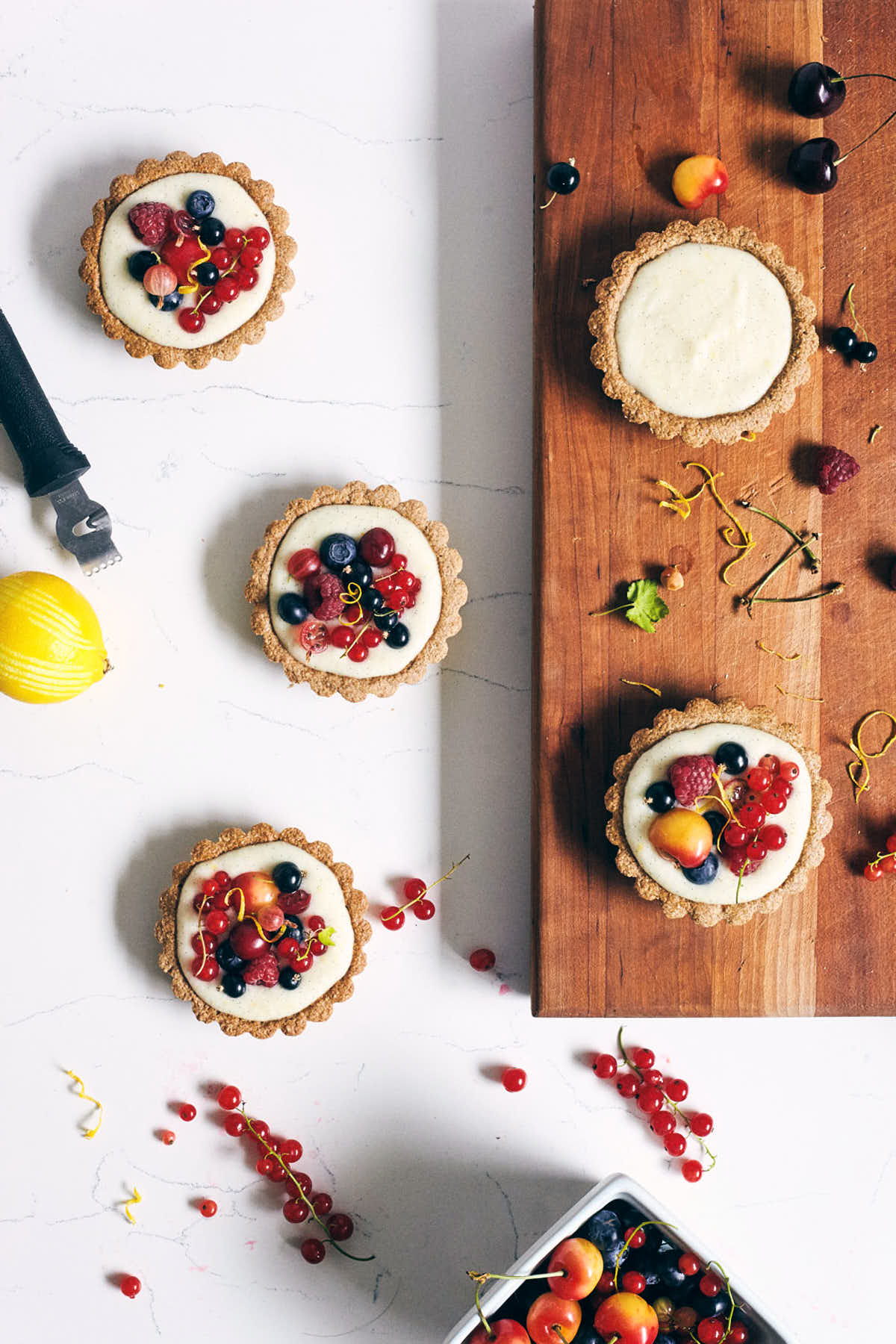 Assembly scene with four five berry tarts on a cutting board and counter