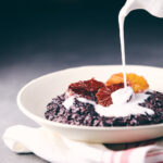 Pouring coconut milk over black rice pudding with blood oranges