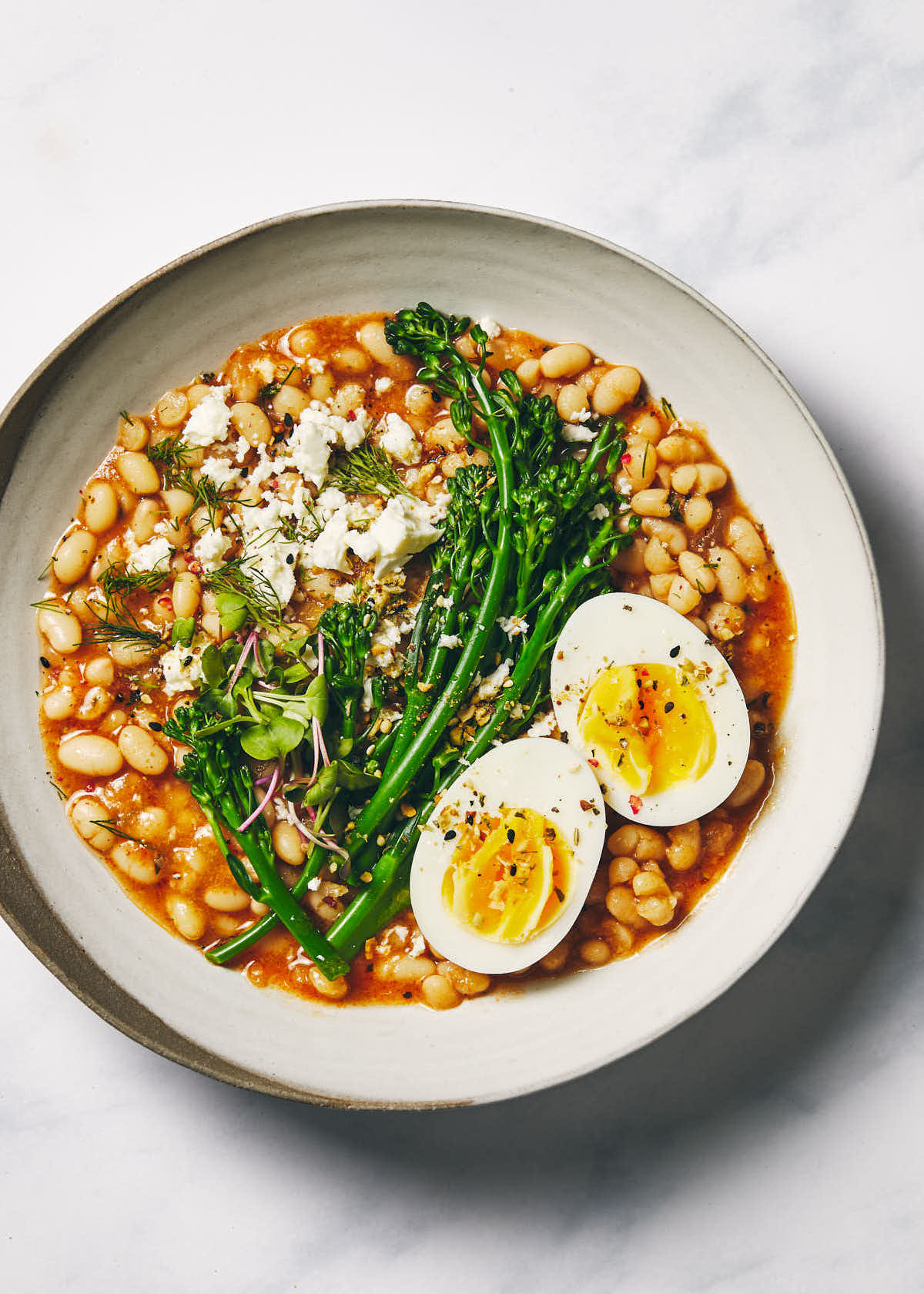Plate of beans topped with an egg and brocollini