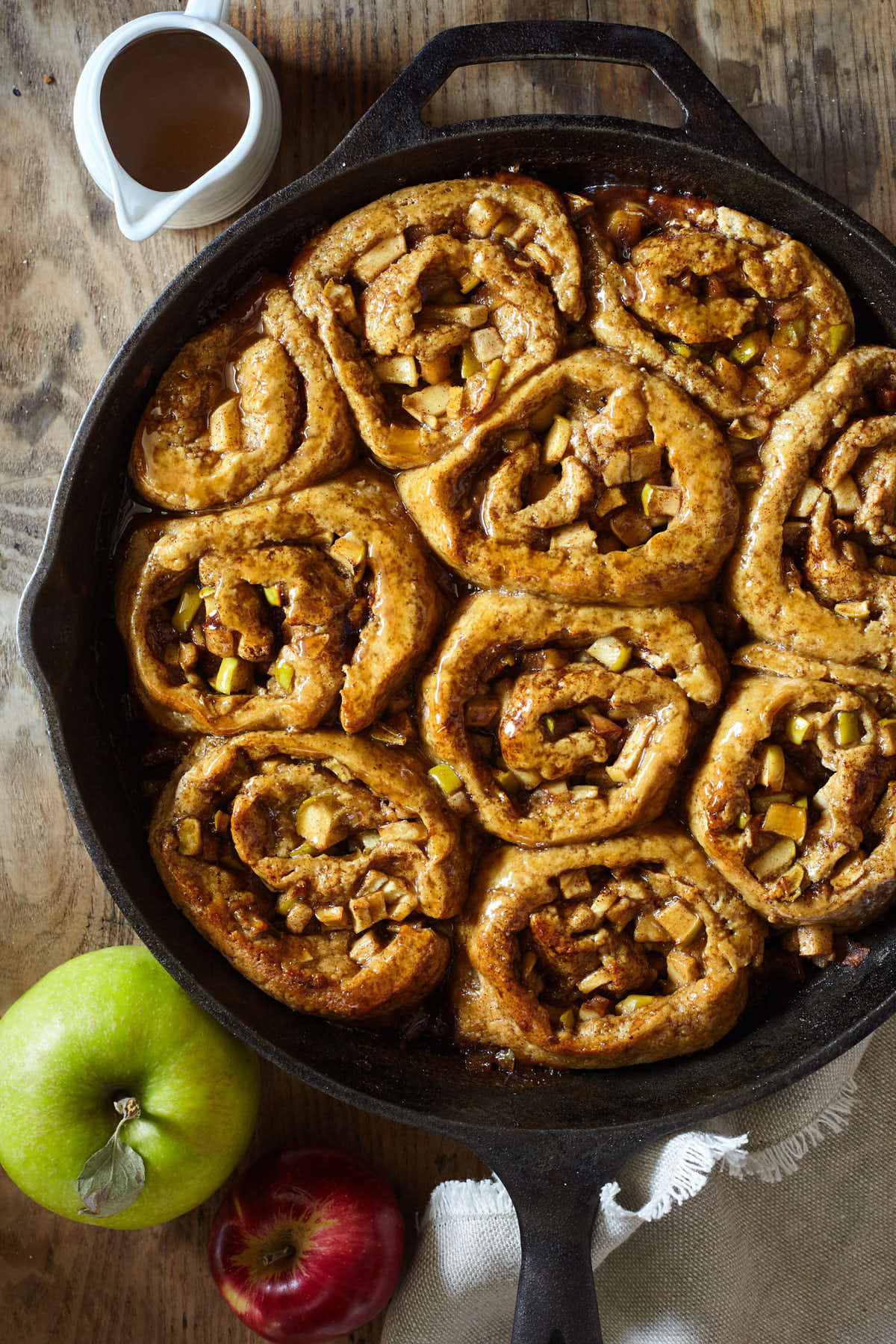 Caramel apple cinnamon buns cooling on a wooden table in a cast iron pan