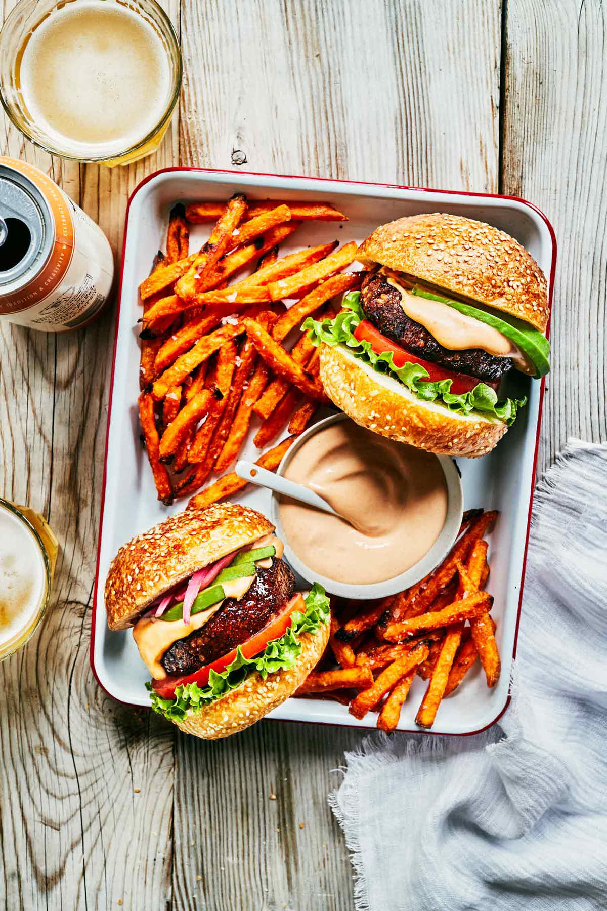 Two chipotle black bean burgers in a serving platter with sweet potato fries and beer