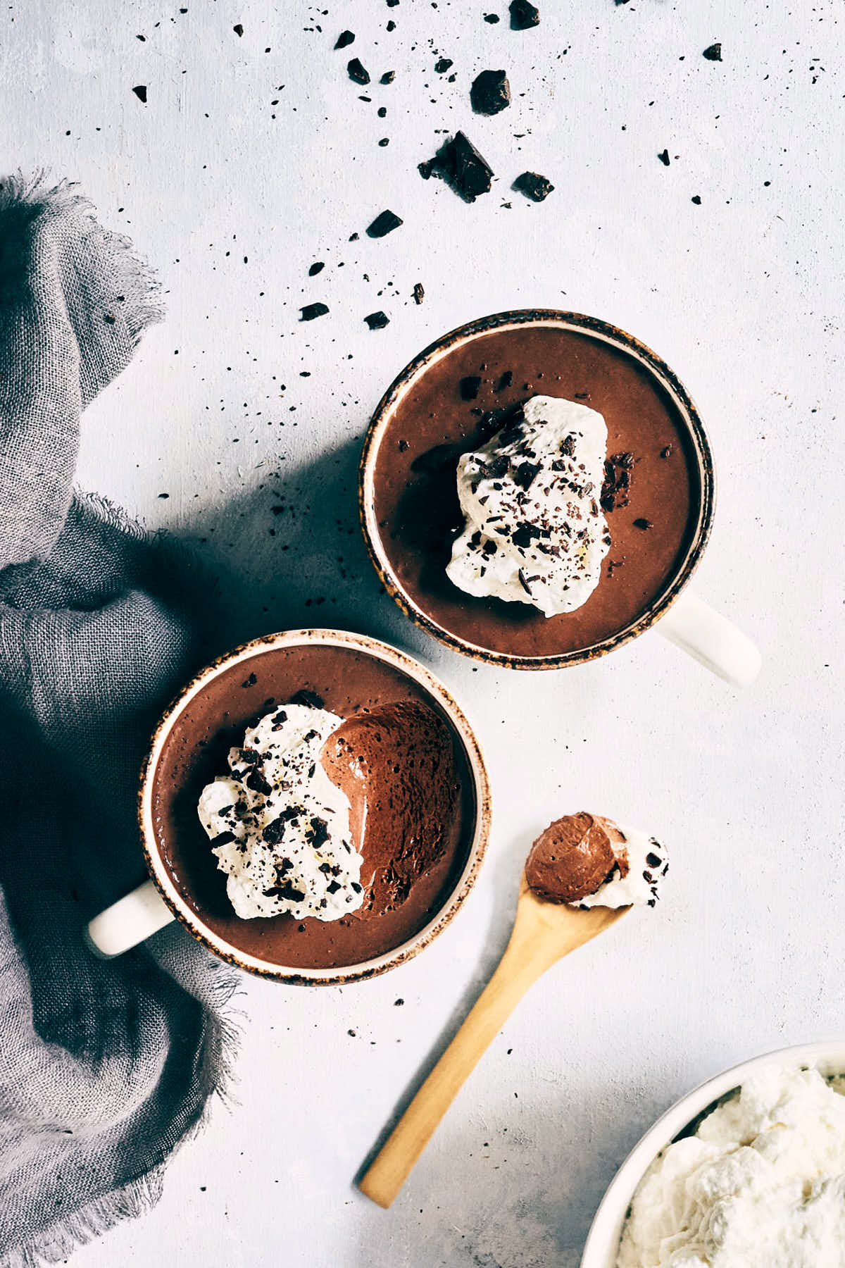 Two cups of chocolate chai pot de creme on a counter with a spoon digging into one
