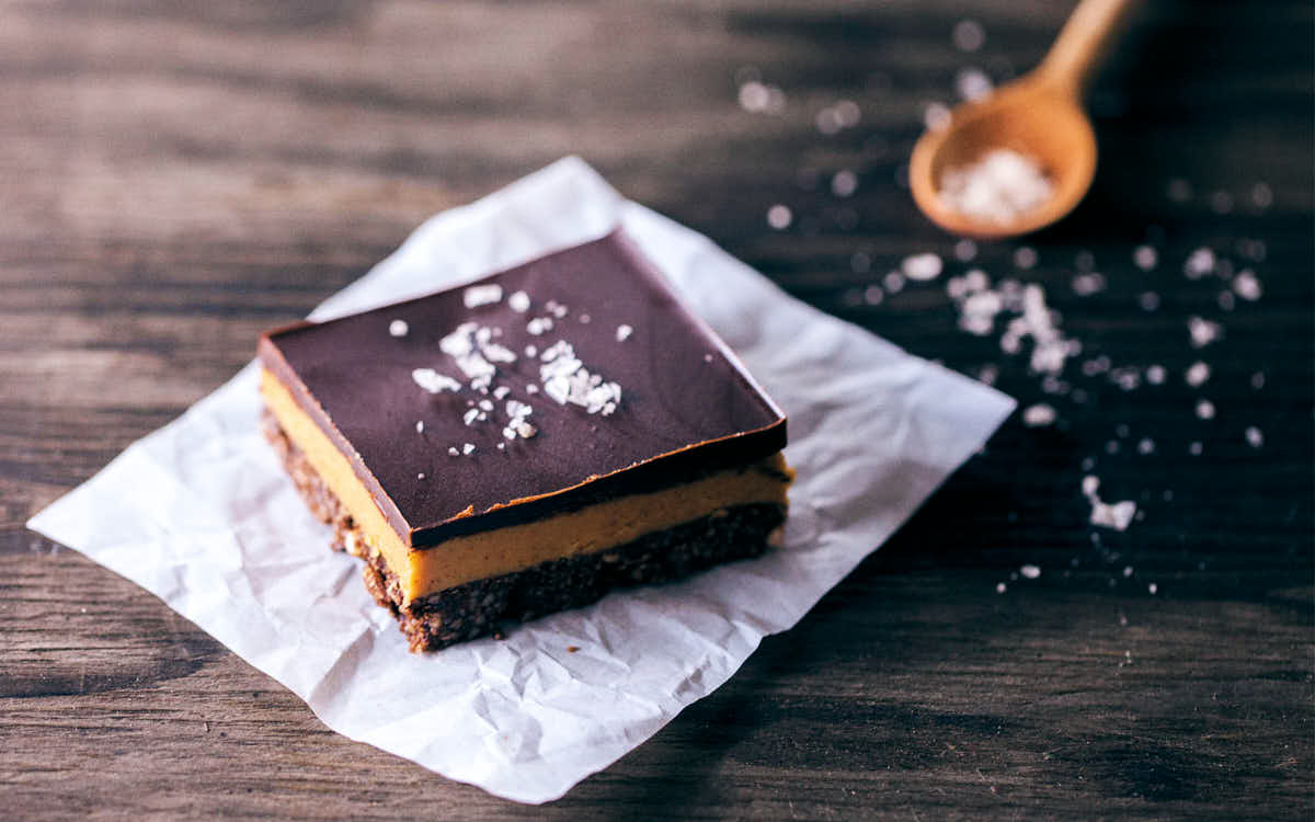 Chocolate peanut butter bars topped with flaky sea salt on white parchment paper