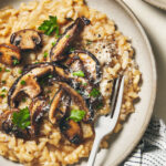 Bowl of mushroom risotto on a wooden surface with a fork digging in
