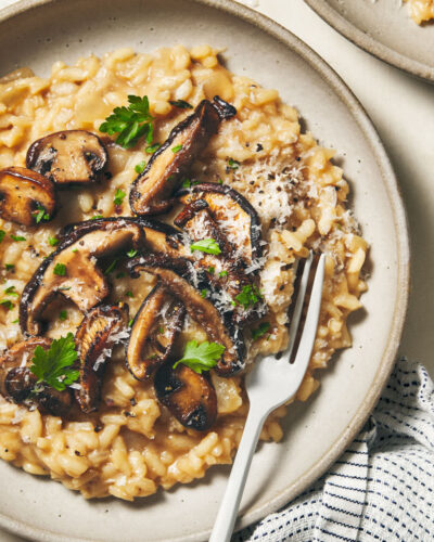 Bowl of mushroom risotto on a wooden surface with a fork digging in