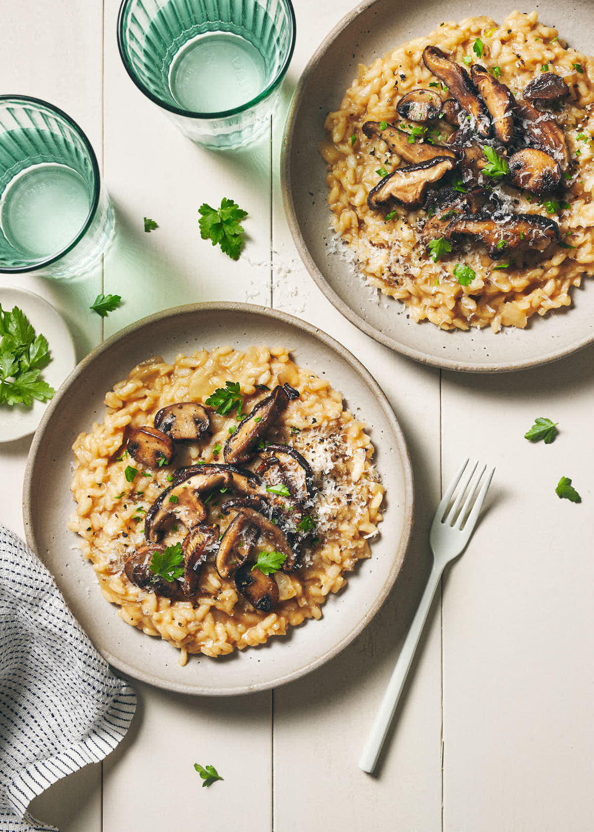 Two bowls of risotto on a wooden table topped with parsley 
