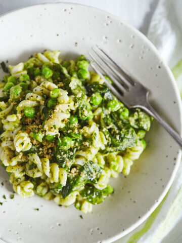 Close up of white bean pesto pasta in a white bowl with fork