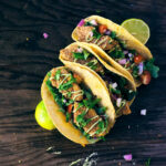 Three crispy squash tacos garnished with limes and cilantro