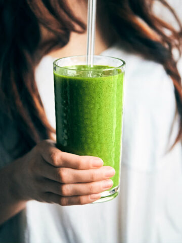 Side view of holding green smoothie with glass straw