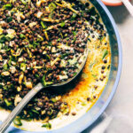 Close up of curry lentil salad over a bed of yogurt with a serving spoon digging in