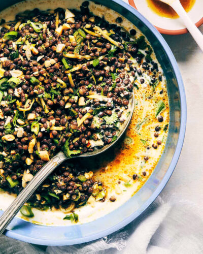 Close up of curry lentil salad over a bed of yogurt with a serving spoon digging in