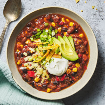 Close up of veggie chili bowl topped with avocado, sour cream, tortilla chips and scallions