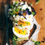 Close up piece of toast with eggs and micro greens on top