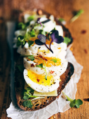 Close up piece of toast with eggs and micro greens on top