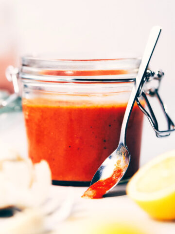Peri-peri sauce in a jar with ingredients like lemon and garlic surrounding it