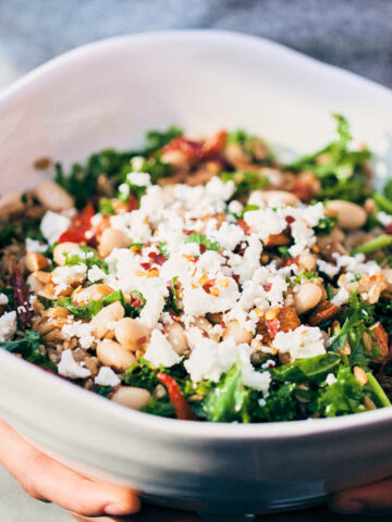 Holding farro pilaf bowl topped with feta and chili flakes