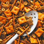 Chex mix cooling in a pan with a white spoon