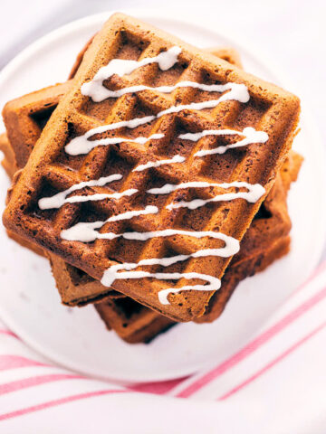 Plate of gingerbread waffles on a white surface topped with maple cinnamon drizzle