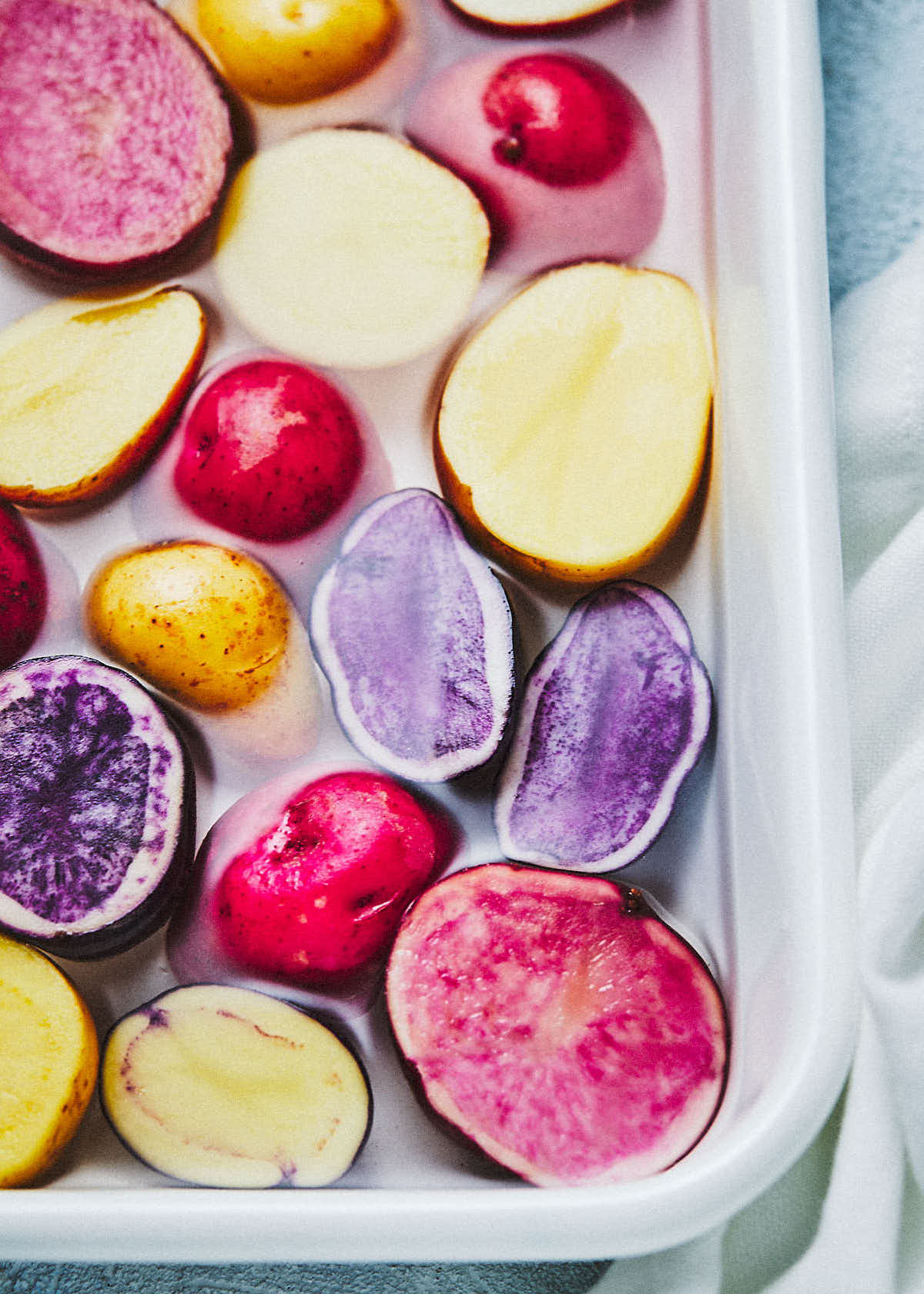 Red, yellow and purple potatoes soaking in a pan of water