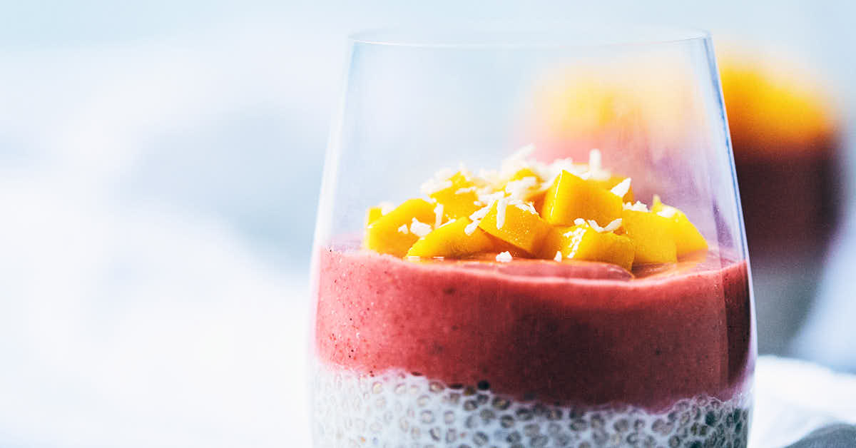 Side view of guava strawberry chia pudding parfait in a glass with chopped mango on top