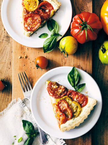 Two pieces of heirloom tomato tart on a serving board with heirloom tomatoes