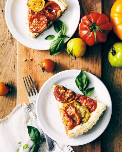 Two pieces of heirloom tomato tart on a serving board with heirloom tomatoes