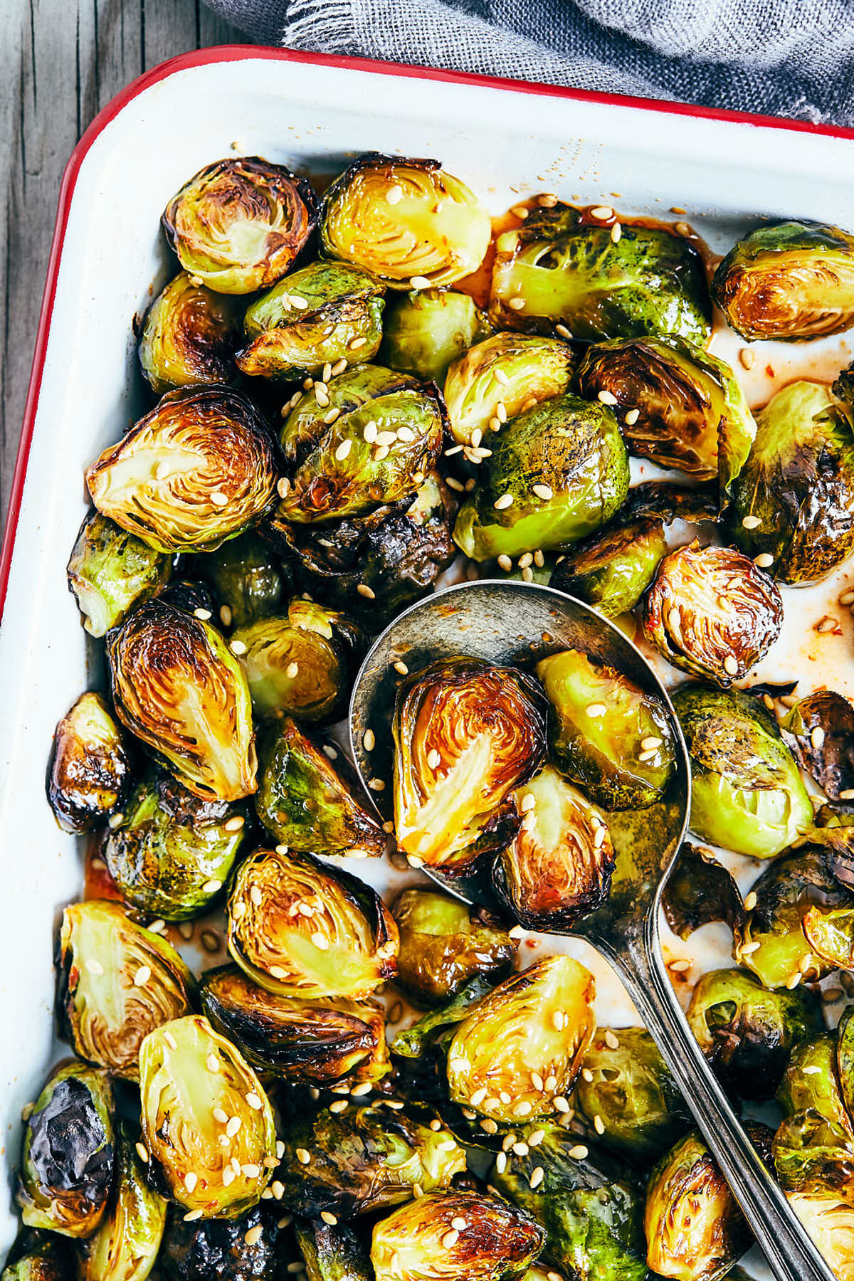Close up of cooked maple sriracha brussels sprouts fresh out of oven in a baking dish and being served by a spoon