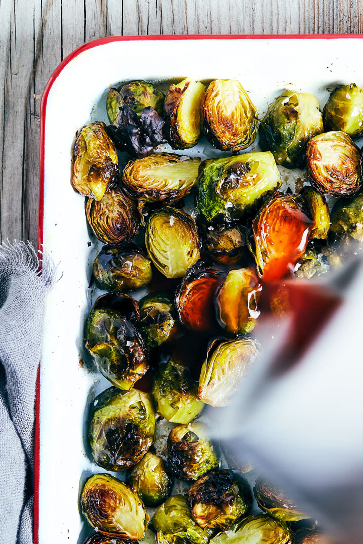 Brussels sprouts being drizzled with maple sriracha dressing after baking