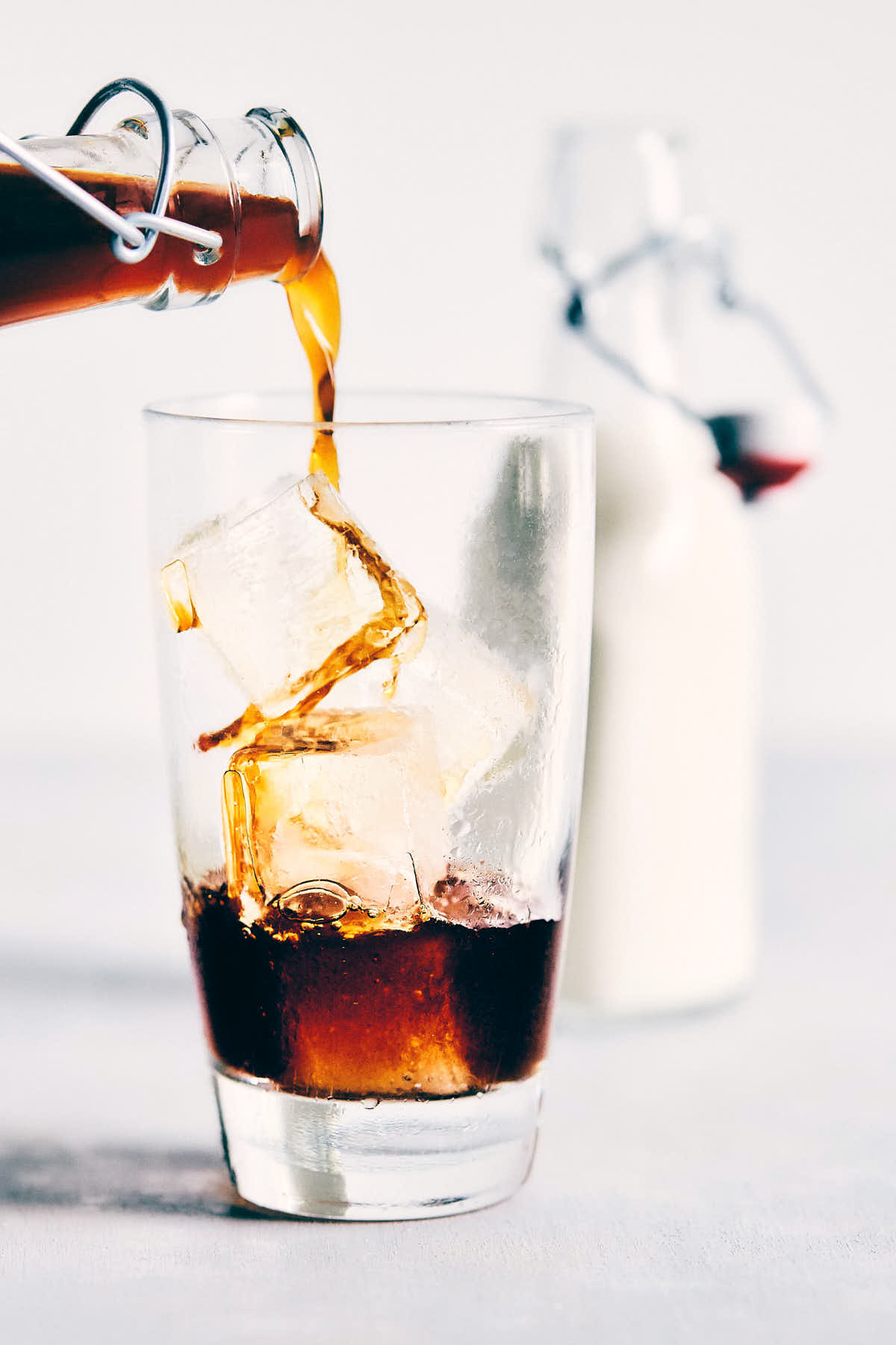 Cold brew coffee being poured over ice in a glass with cream in the background