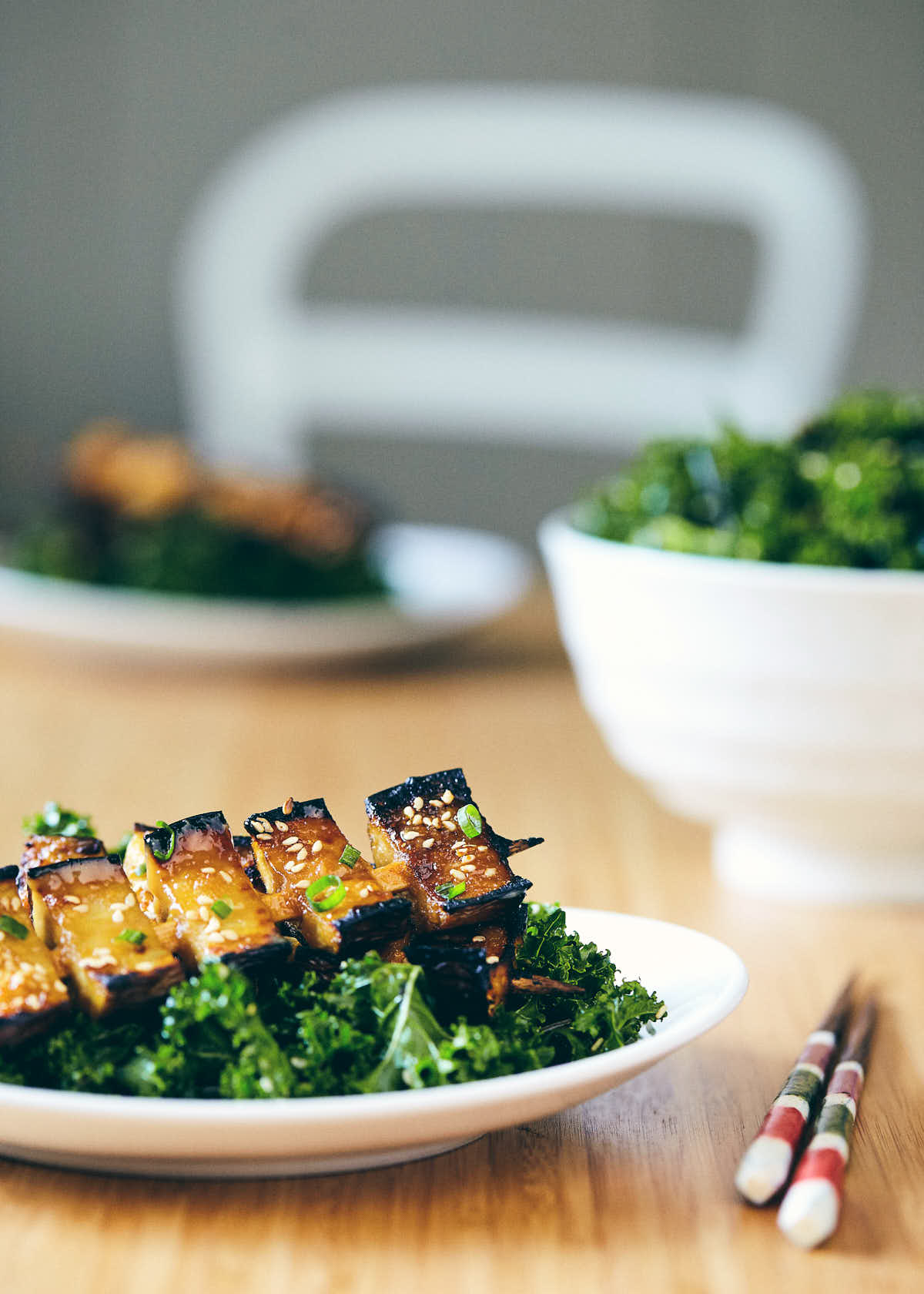 Side view of table scene with miso glazed eggplants and kale seaweed salad in a large bowl