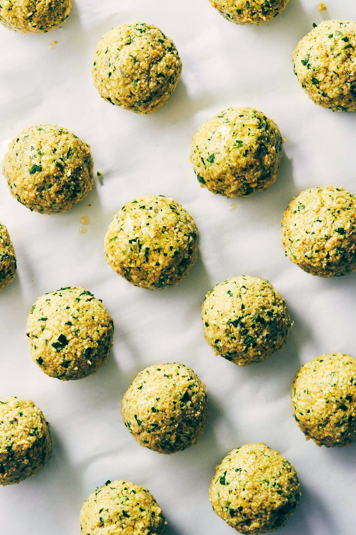 Falafel balls rolled and being oiled on a baking sheet lines with parchment paper