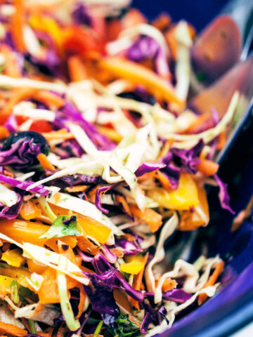 Digging into serving bowl of rainbow slaw with serving spoons