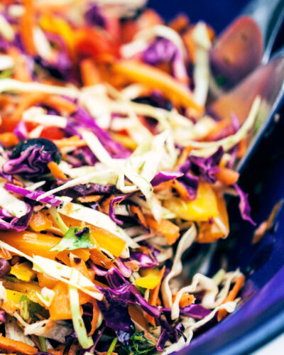 Digging into serving bowl of rainbow slaw with serving spoons