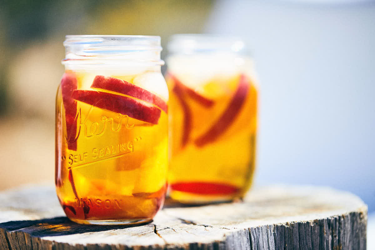 Two mason jars of red rooibos tea sangria with ice and stone fruit