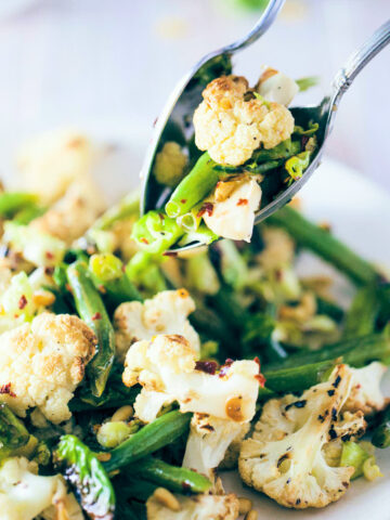 Scooping roasted cauliflower and brussels sprout salad with serving spoons
