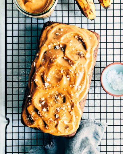 Salted caramel banana bread on a cooling rack after it has been topped with salted caramel and flaky sea salt