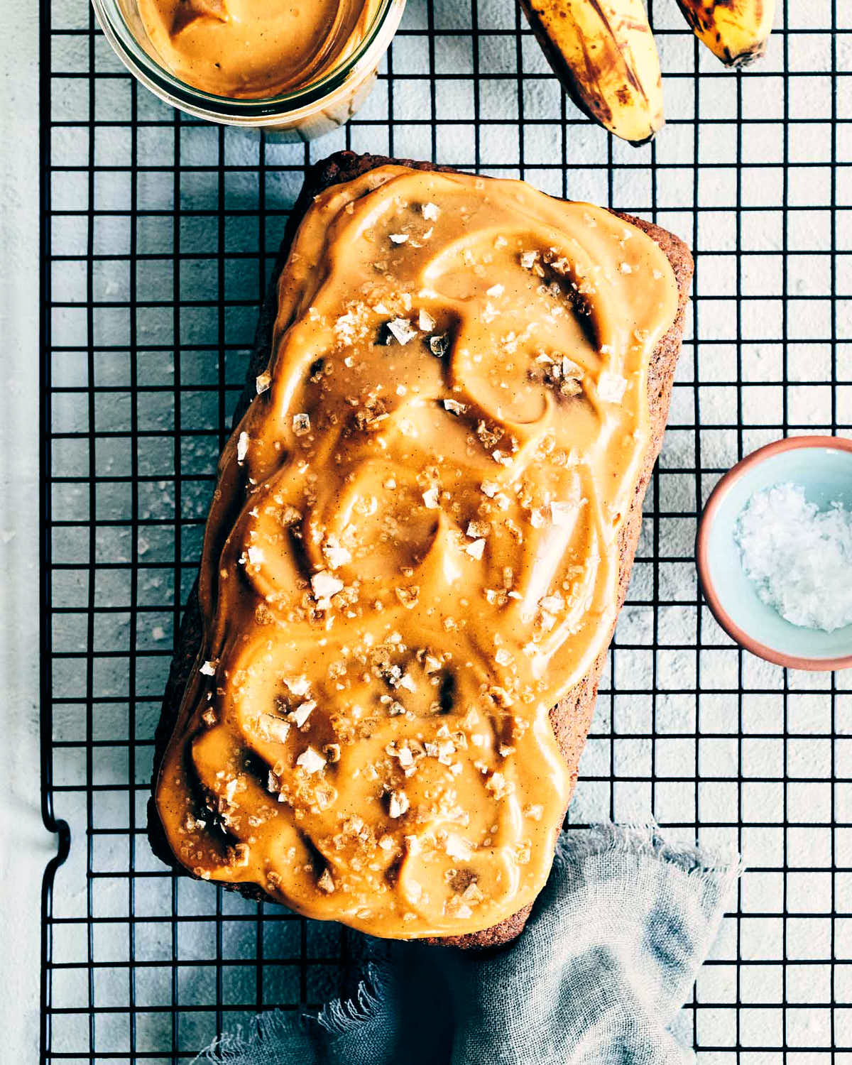 Salted caramel banana bread on a cooling rack after it has been topped with salted caramel and flaky sea salt