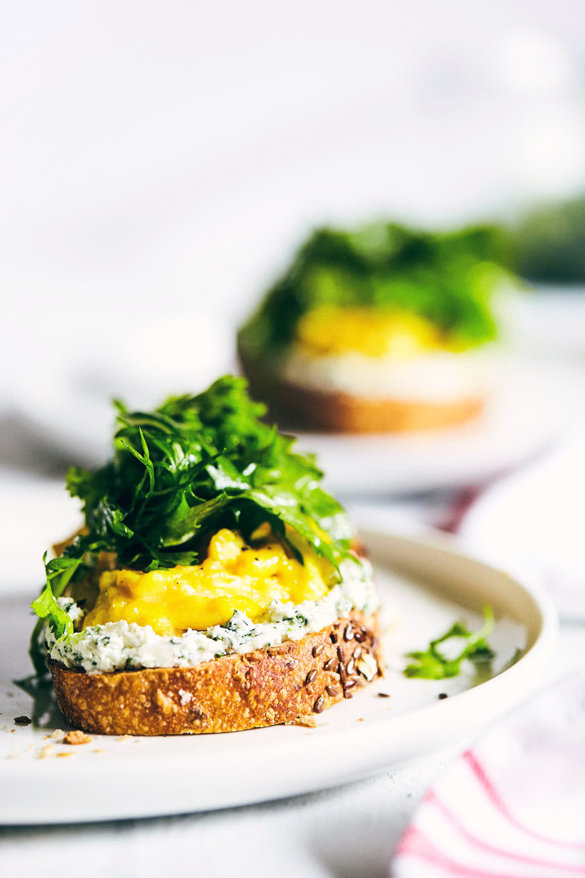 Side view of scrambled eggs and goat cheese toast topped with fresh arugula