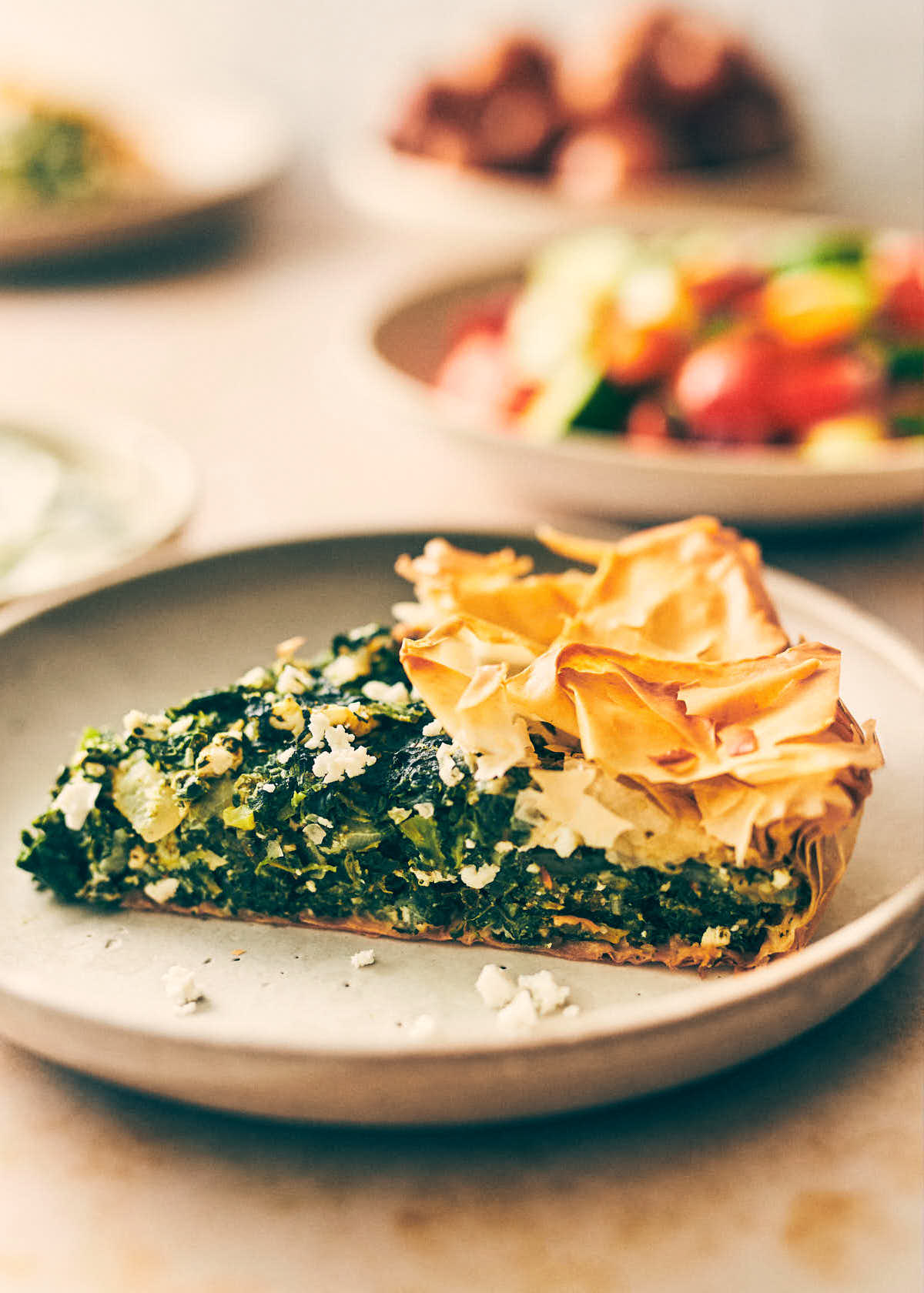 Slice of spanakopita on a plate with greek salad in the background