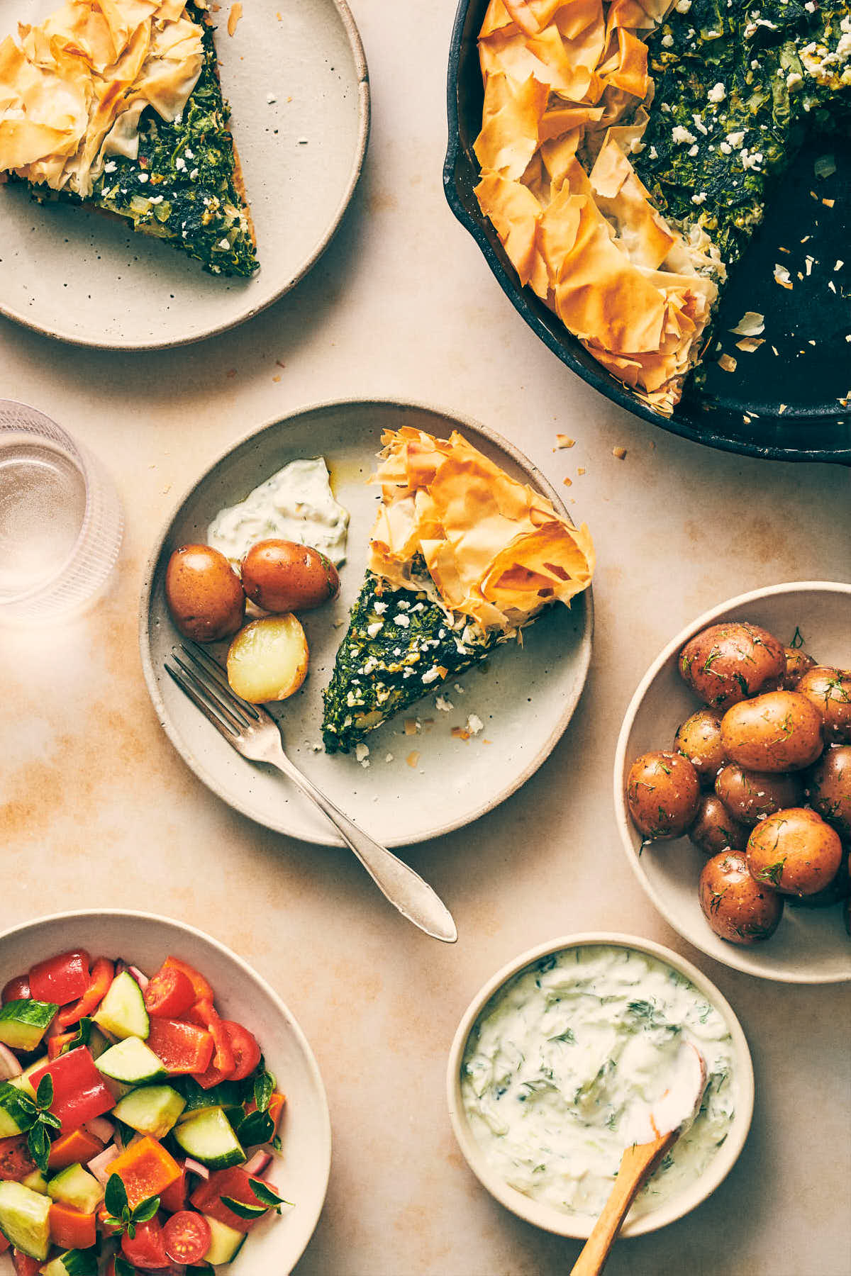 Plates with slices of spanakopita, roasted potatoes and Greek salad
