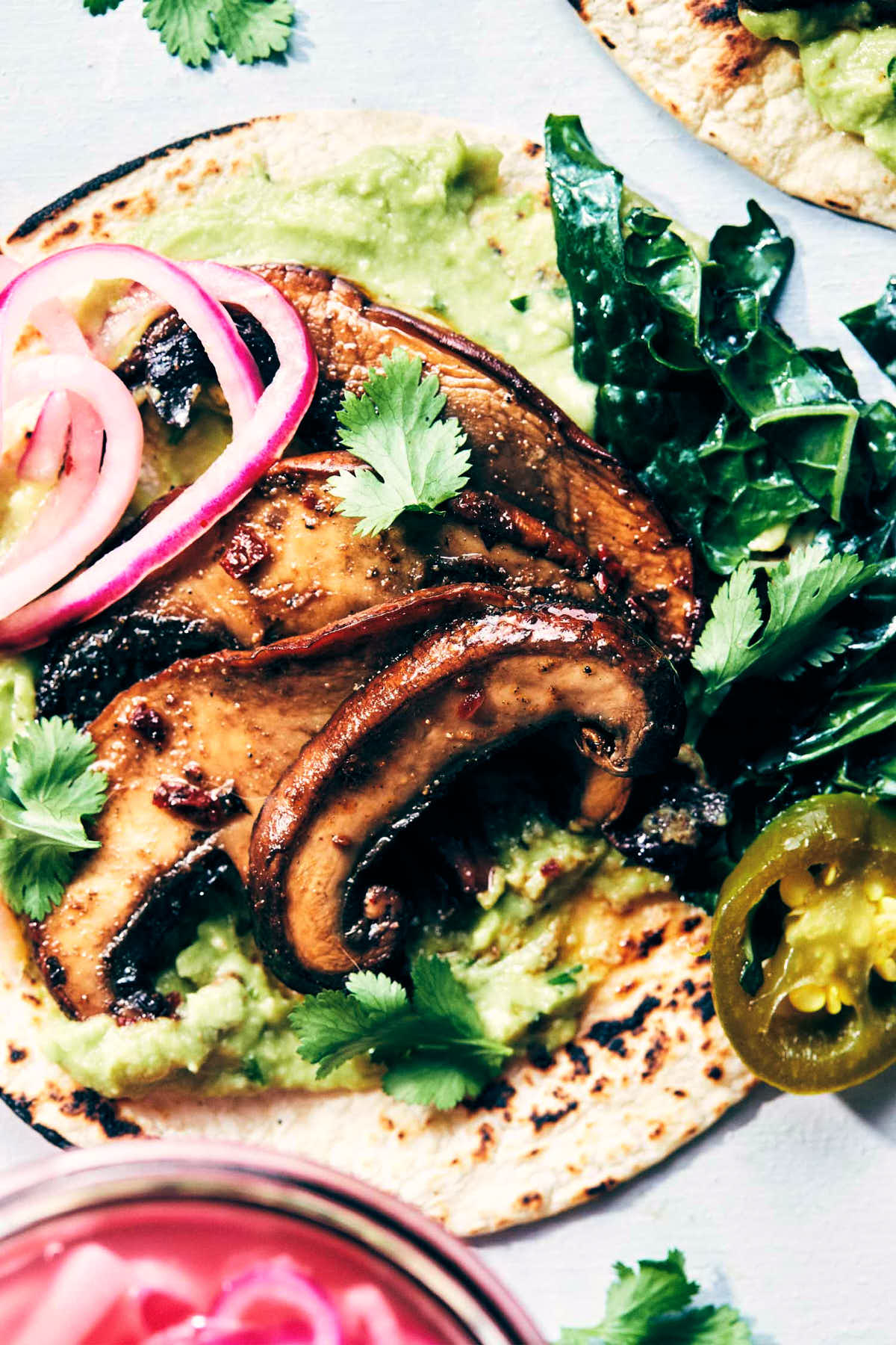 Close up shot of fully dressed taco featuring mushrooms, kale, avocado and pickled red onions