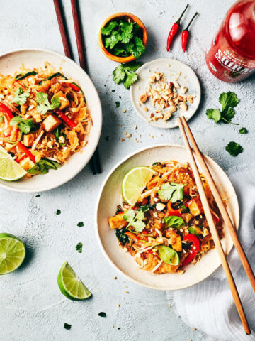 Two dishes of spaghetti squash pad Thai with garnishes like peanuts, cilantro, and lime