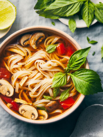 Close up bowl of thai hot and sour soup with thai basil and limes