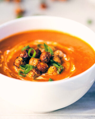 Side view of tomato ginger soup topped with crispy chickpeas and scallions