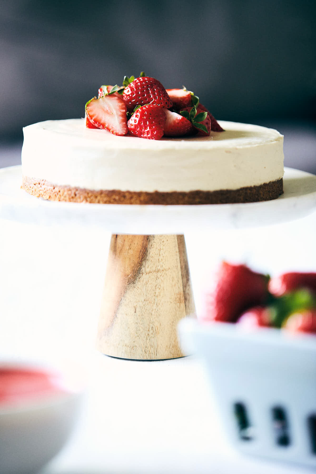 Side view of cheesecake on a cake stand with washed strawberries in the foreground