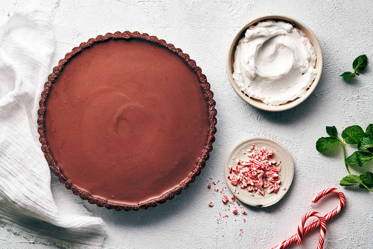 Baked chocolate peppermint tart sitting on the counter about to be topped with whipped cream and candy cane