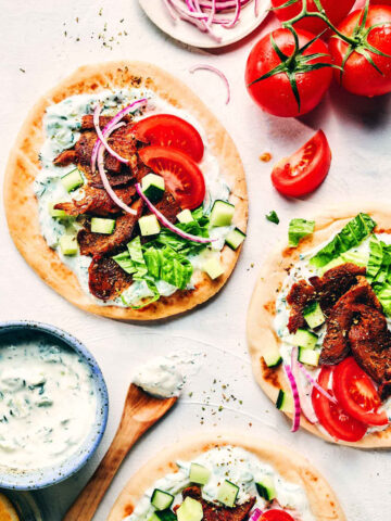 Greek gyros on a counter topped with fresh veggies and tzatziki