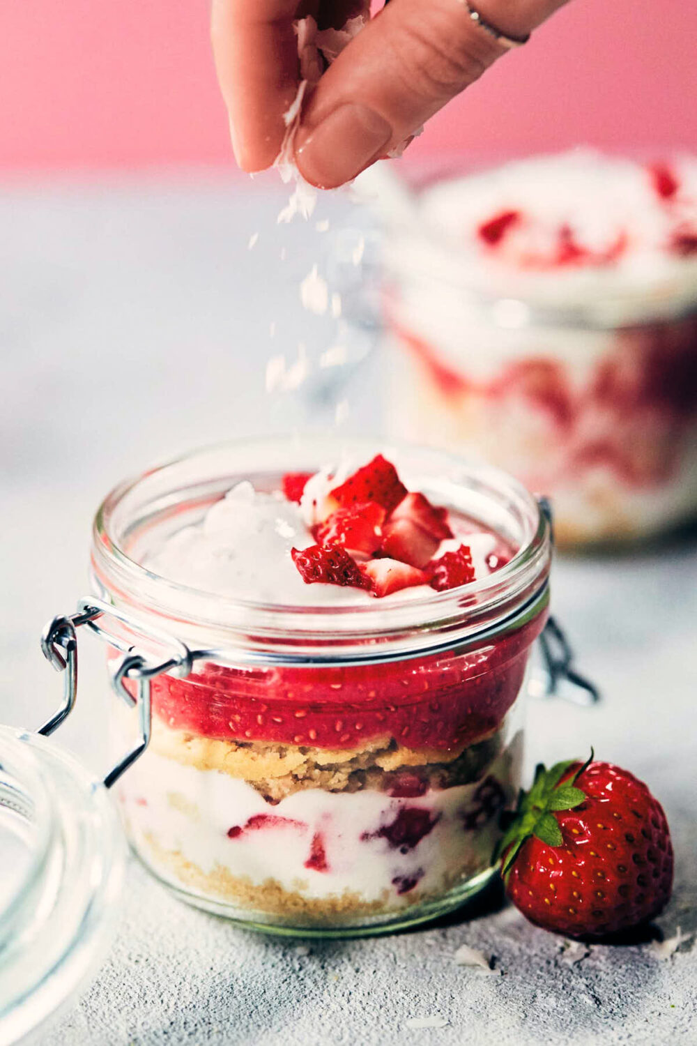 Vegan strawberry shortcake in a jar being sprinkled with optional coconut flakes.